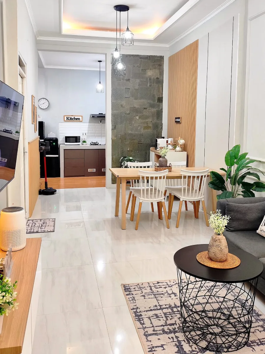 Tata ruang terbuka bergaya minimalis yang memperlihatkan ruang tamu, ruang makan dengan kursi putih, dan dapur bersih di bagian belakang.