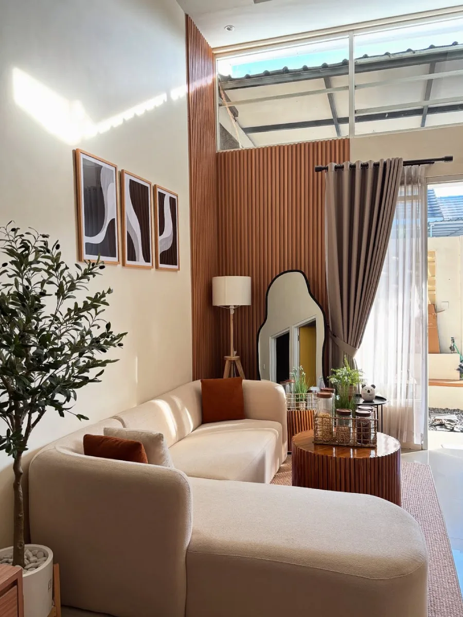 Ruang tamu bergaya Skandinavia bernuansa hangat yang disinari cahaya matahari alami, lengkap dengan pintu kaca terbuka dan tanaman zaitun tiruan.