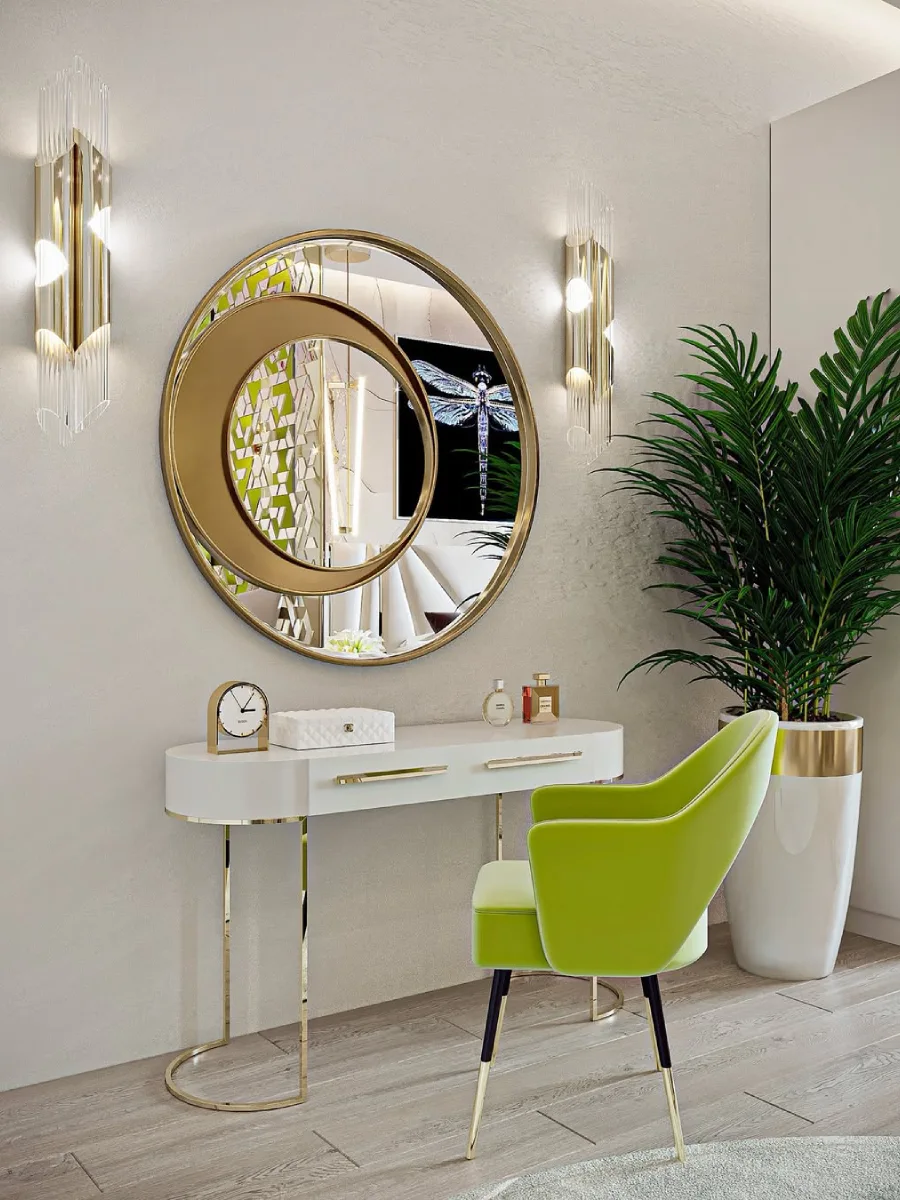 Meja rias modern berwarna putih dan emas dengan kursi beludru hijau limau, cermin bulat besar, dan tanaman pot.