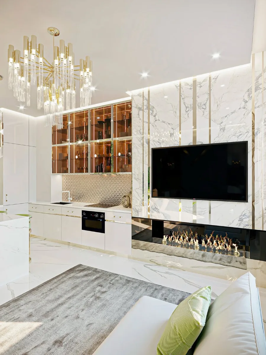 Ruang tamu dan dapur terbuka yang mewah menampilkan dinding TV marmer berurat emas dengan perapian linier, dapur putih mengkilap, unit lemari kaca berbingkai perunggu, dan lampu gantung kristal emas.