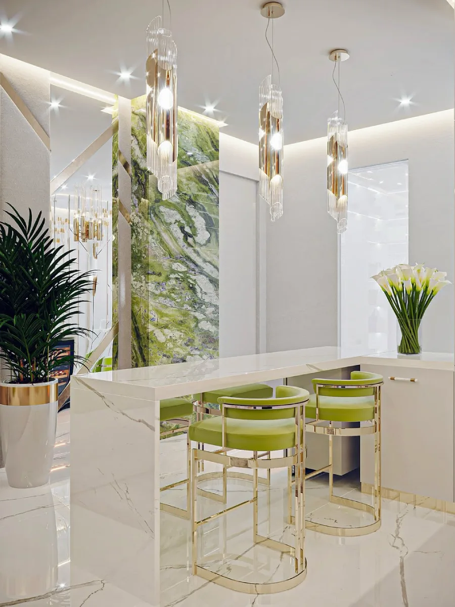 Bar dapur modern dengan meja marmer putih, kursi bar beludru hijau limau, dinding aksen marmer hijau zamrud, dan lampu gantung silindris.