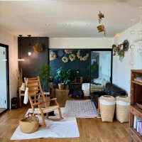 Ruang tamu dengan sentuhan natural dan rustic menampilkan kursi goyang kayu dinding aksen gelap berhias bunga kering serta keranjang anyaman untuk penyimpanan dan tanaman hias