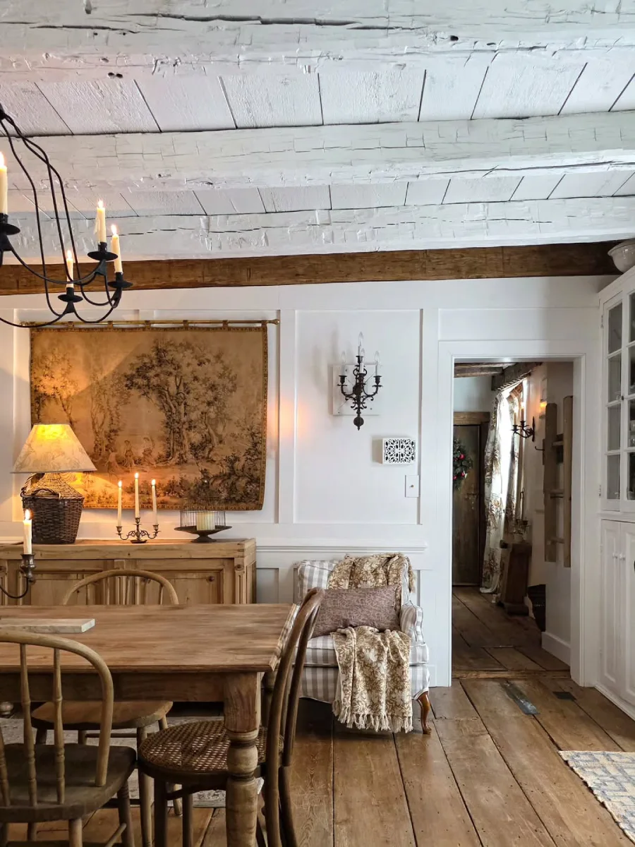 Ruang makan bergaya rustic dengan balok atap kayu bercat putih meja makan kayu alami kursi bermotif kotak-kotak dan bufet kayu antik yang diterangi cahaya lilin