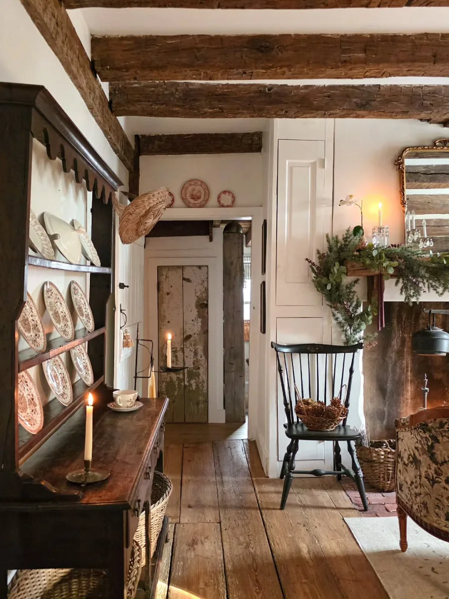 Lorong rumah bernuansa rustic klasik dengan rak dinding kayu berisi piring hias antik kursi kayu hitam dan perapian bata dengan dekorasi tanaman hijau