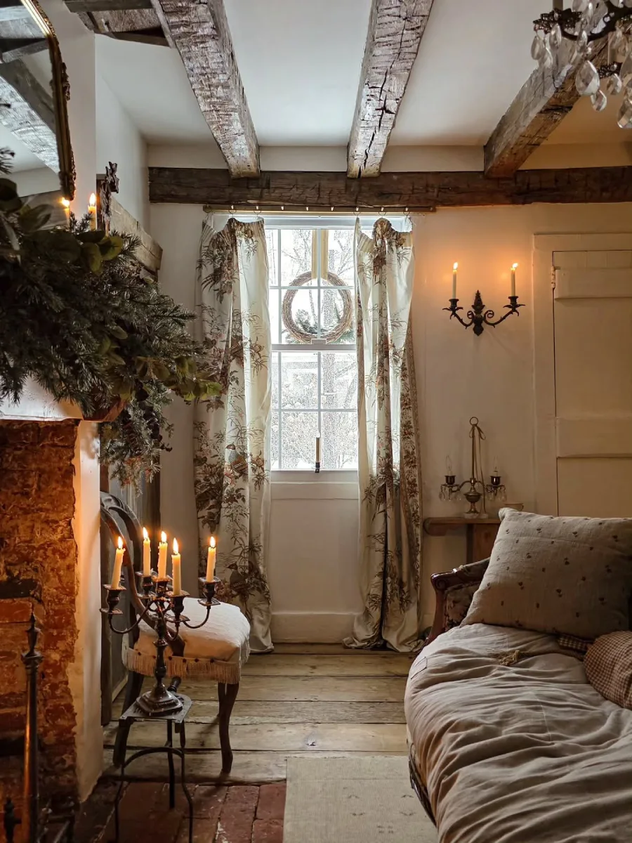 Area bersantai yang hangat di dekat perapian bata dengan tempat duduk berlapis kain linen tirai bermotif klasik dan tempat lilin tembaga yang menyala