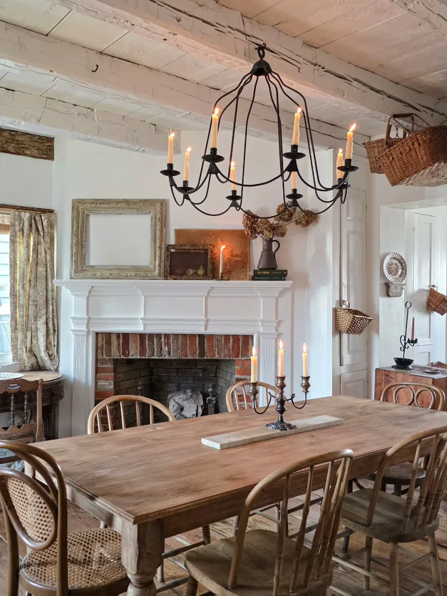 Ruang makan berdesain rustic menonjolkan meja makan kayu solid kursi kayu melengkung perapian bata berbingkai putih dan lampu gantung besi tempa bergaya lilin