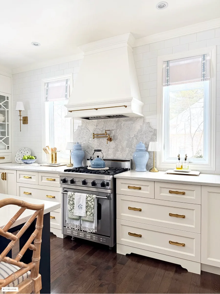 Kompor baja tahan karat di dapur dengan backsplash marmer tudung kompor putih keran air kuningan dan dekorasi guci biru yang simetris