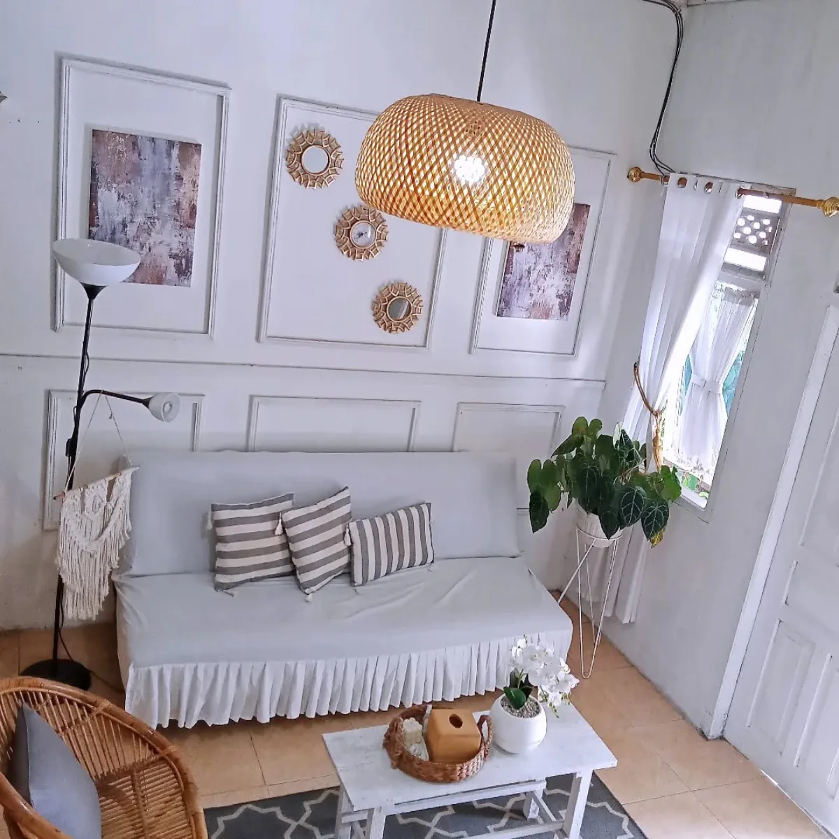 Interior ruang santai bergaya bohemian minimalis dengan cat dinding warna putih gading, dekorasi dinding panel, dan lampu rotan gantung.