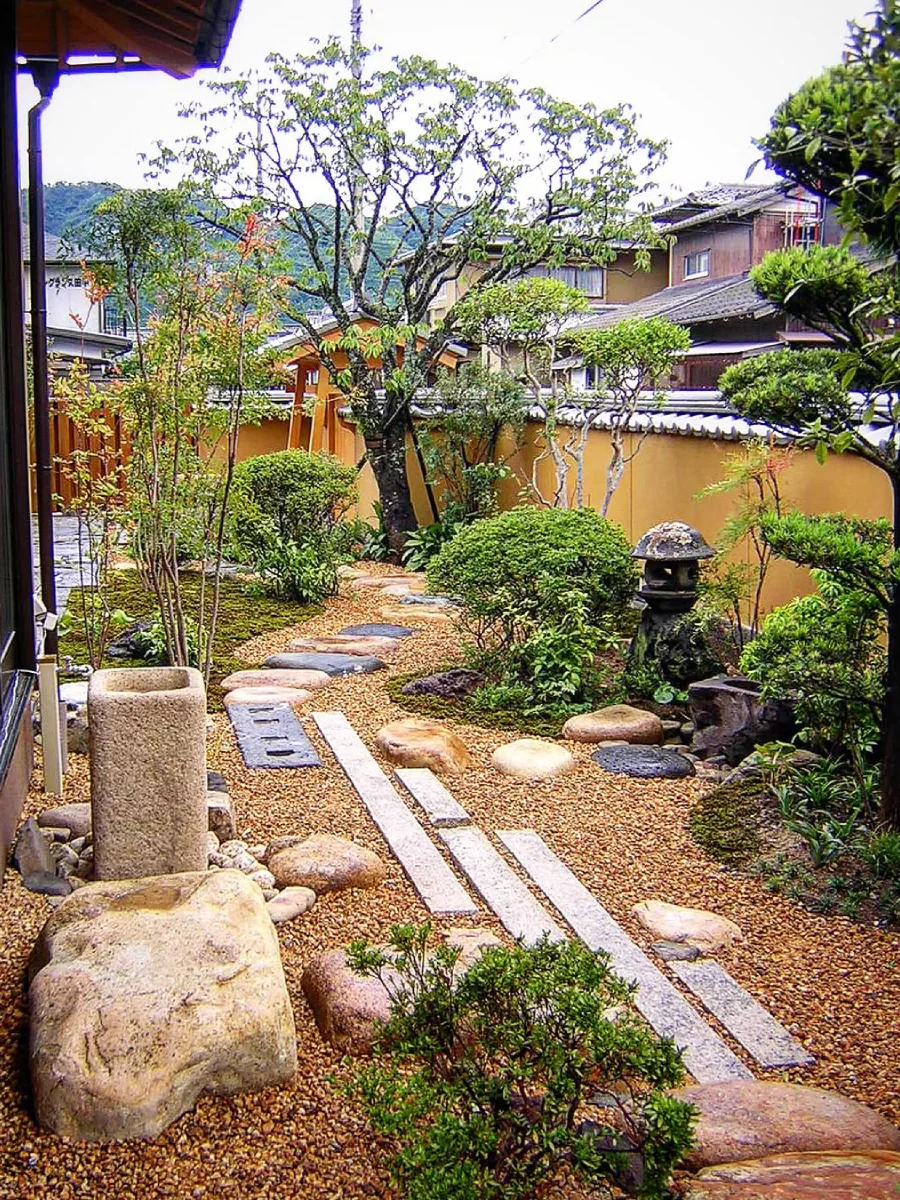 Taman Jepang dengan lentera batu dan jalur setapak yang mengarah ke area hijau.