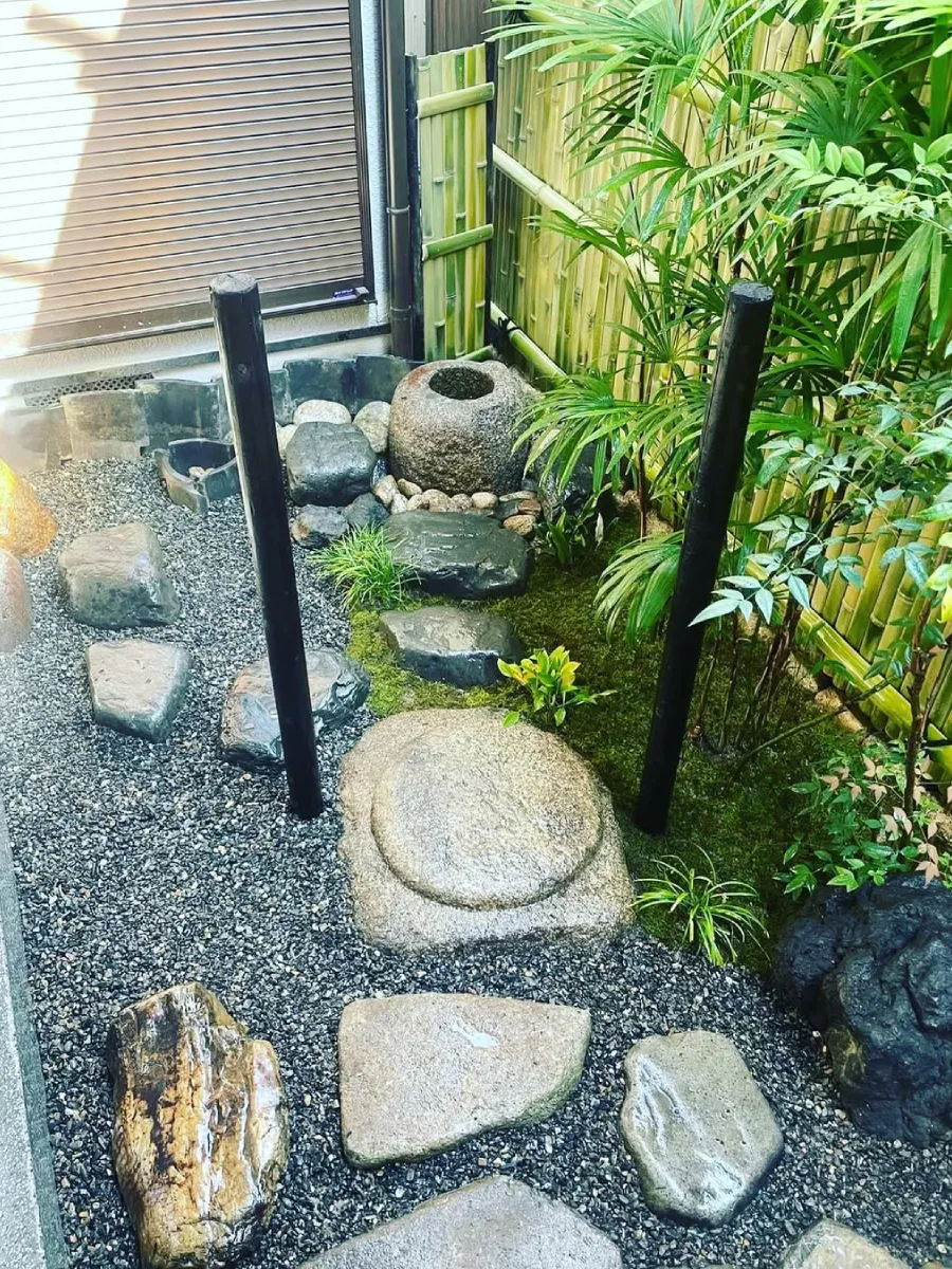 Taman Jepang hijau dengan lumut, batu besar, dan suasana teduh ala hutan Jepang.