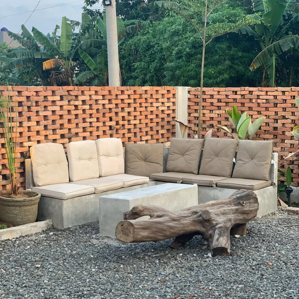 Area santai taman kering belakang rumah bergaya industrial rustic dengan dinding bata merah ekspos, tempat duduk beton (concrete bench), dan aksen kayu log alami.