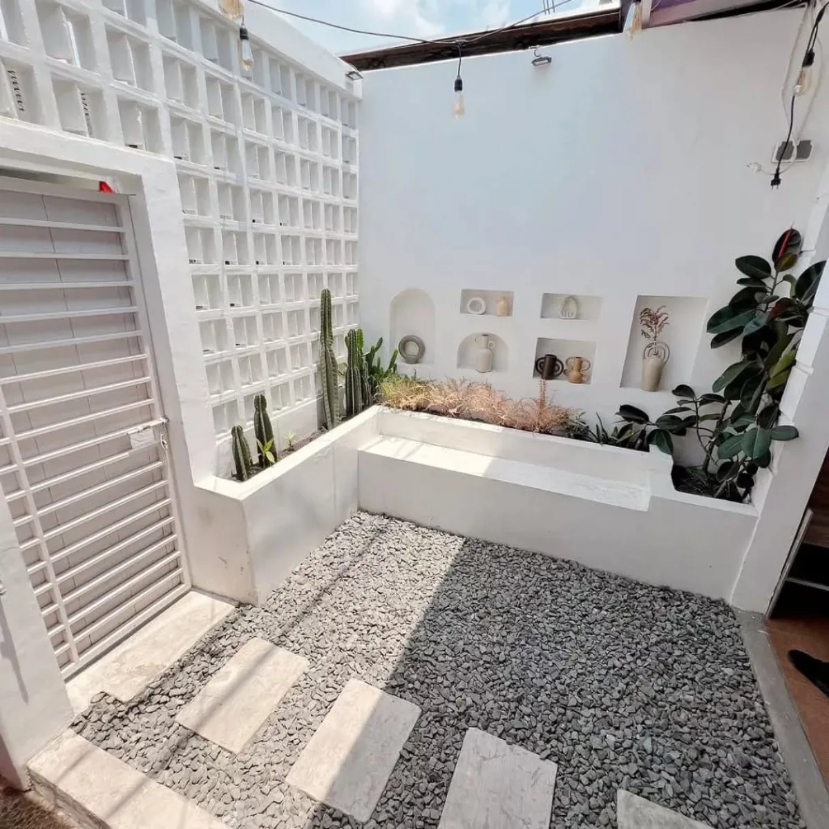 Inspirasi taman kering courtyard estetik nuansa putih (all-white) dengan dinding roster, lantai kerikil abu-abu, kaktus koboi, dan area duduk santai yang instagramable.