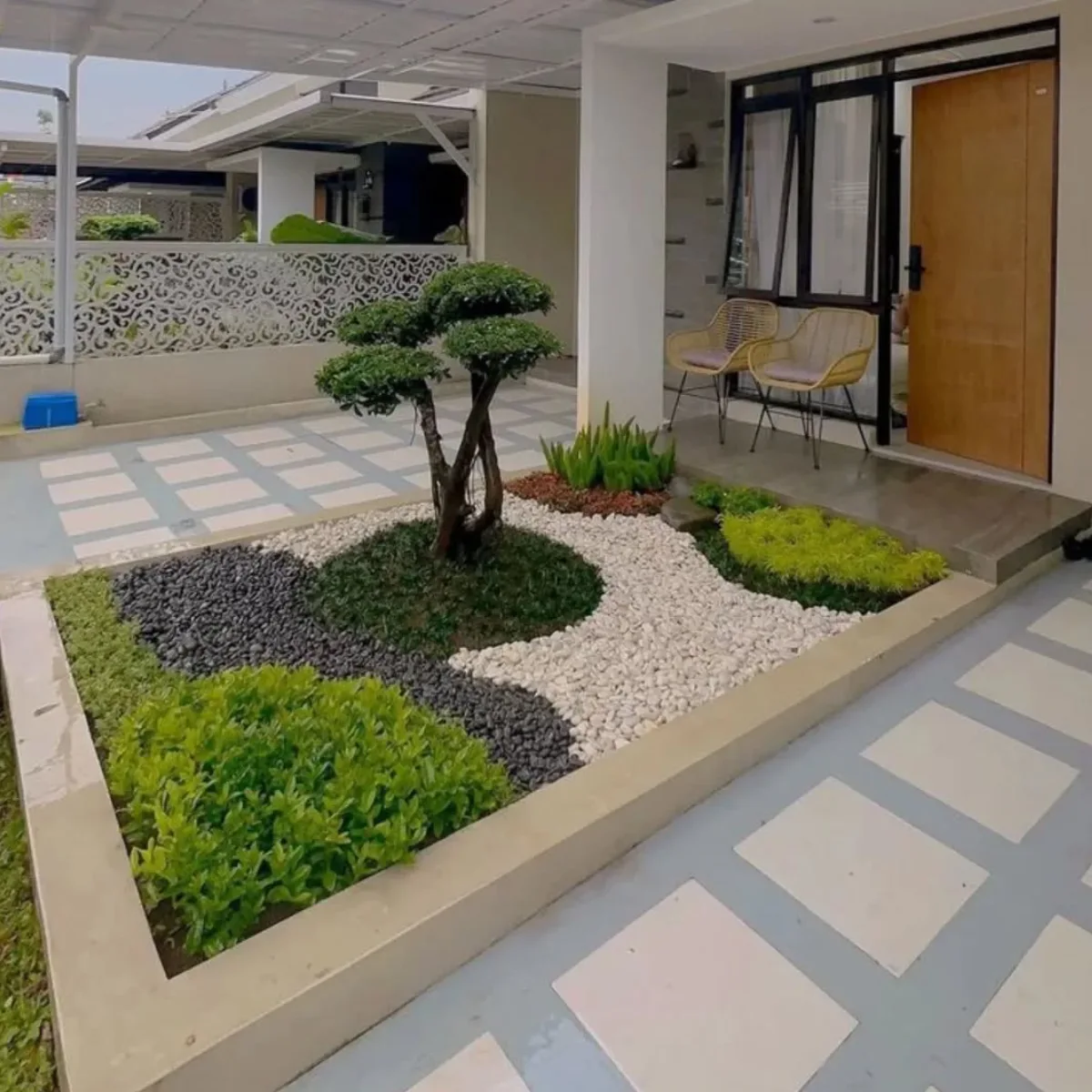 Desain taman kering minimalis depan rumah dengan pohon bonsai artistik, pola lantai batu koral hitam putih melengkung, dan area teras santai modern.