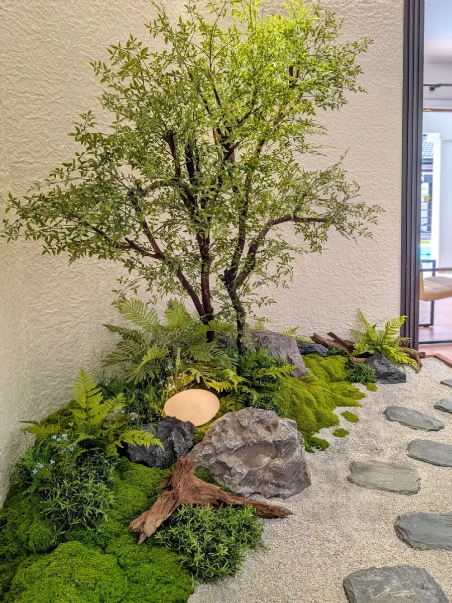 Pojok taman kering (dry garden corner) nuansa hutan mini dengan pohon ranting, kombinasi batu karang, pasir silika, dan pencahayaan hangat untuk interior rumah.