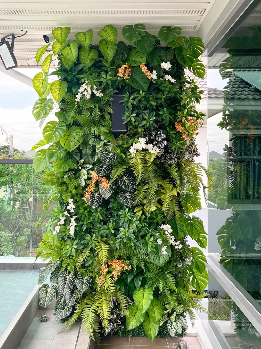 Taman vertikal hijau dengan berbagai jenis tanaman hias daun dan bunga, dipasang pada dinding outdoor rumah modern untuk menciptakan suasana segar dan estetis.