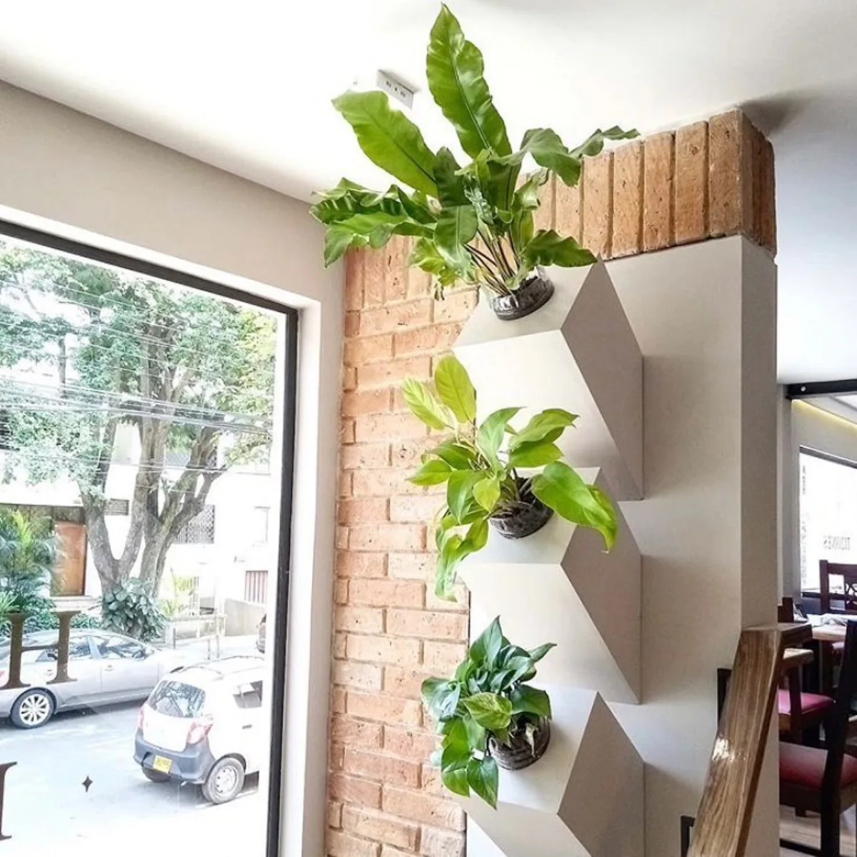 Rak dinding geometris berwarna putih dengan pot-pot tanaman hijau yang ditata vertikal di sudut ruangan bergaya industrial.