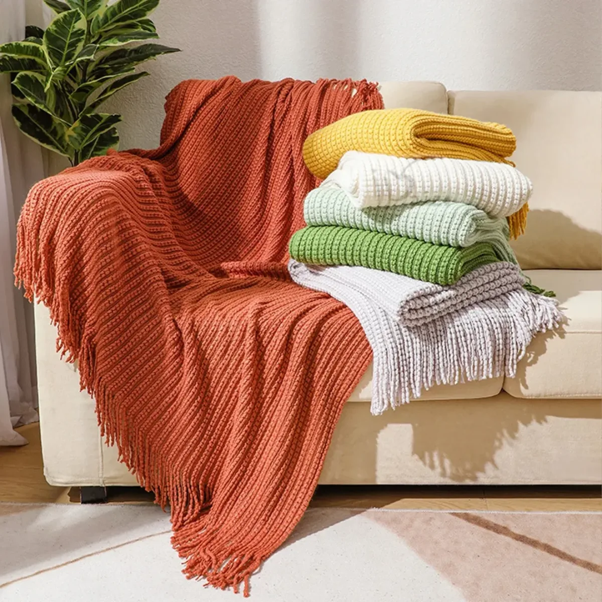 Tumpukan selimut rajut warna-warni yang ditata cantik di atas sofa krem untuk menambah tekstur dan kenyamanan ruang tamu