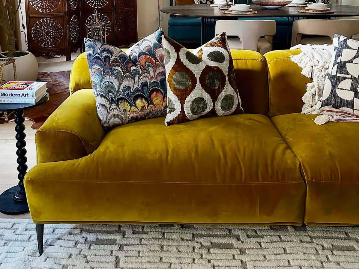 Sofa velvet warna kuning mustard dengan bantal motif di ruang tamu bergaya modern bohemian