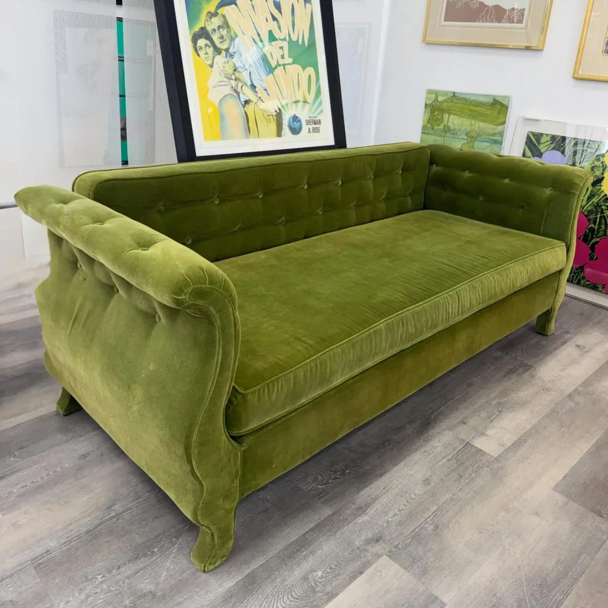 Sofa bergaya klasik chesterfield yang dilapisi bahan velvet atau beludru berwarna hijau lumut yang mewah dan berkilau, memiliki detail kancing atau tufting pada bagian sandaran serta lengan sofa melengkung yang elegan.