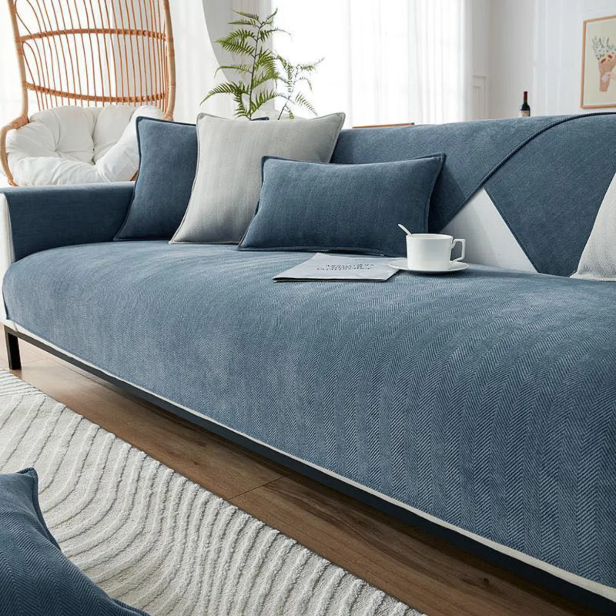 Sofa panjang yang dibalut dengan bahan chenille berwarna biru dengan tekstur pola chevron yang khas dan tebal, memberikan kesan hangat dan nyaman, dilengkapi dengan beberapa bantal pelengkap dan secangkir kopi di atasnya.