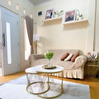 Ruang tamu kecil dengan sofa krem, meja kopi bundar minimalis, karpet netral, dan dekorasi sederhana yang membuat ruangan terlihat rapi dan nyaman.