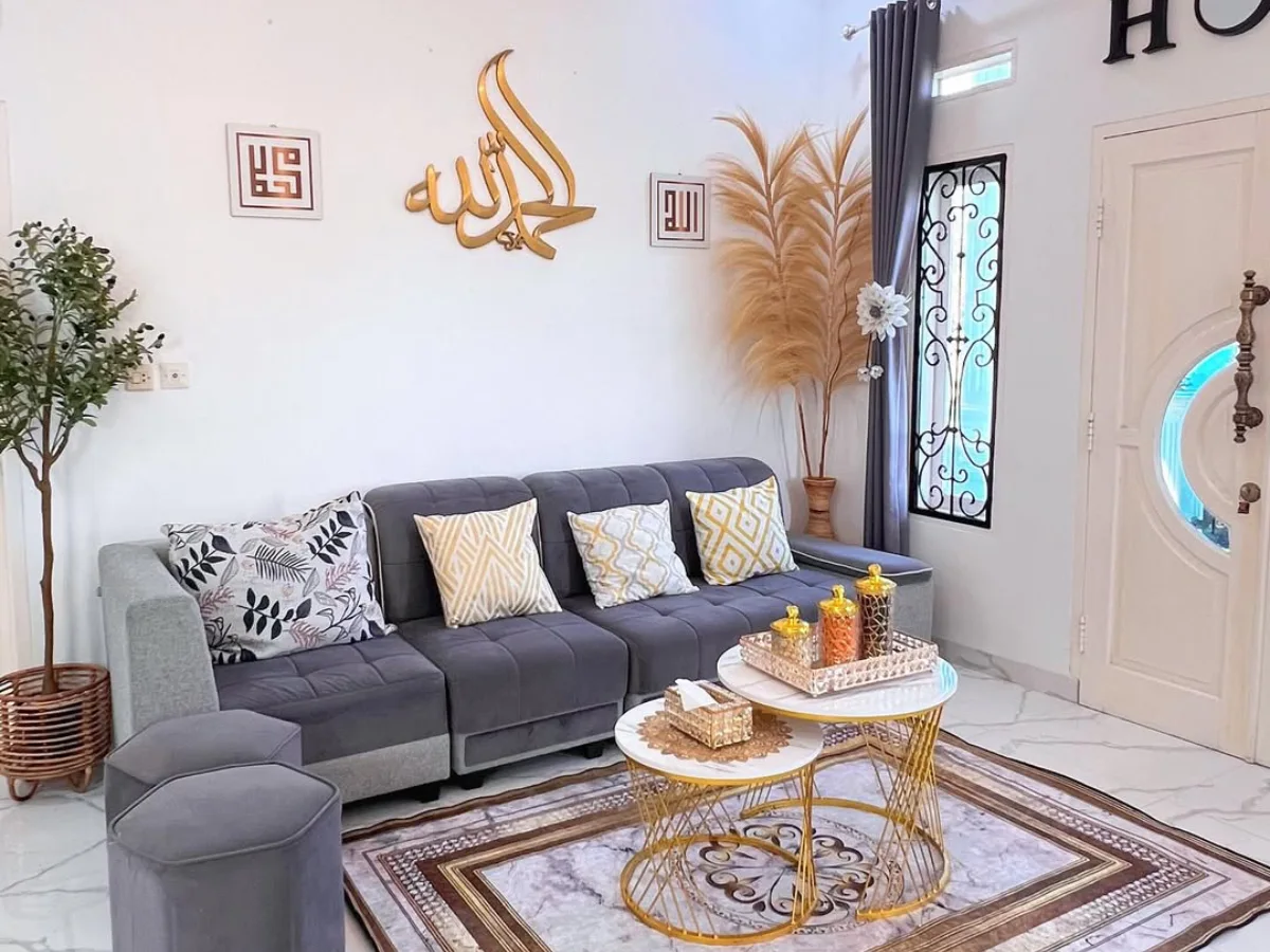 Ruang tamu minimalis dengan sofa abu abu berbentuk L, meja bundar emas, karpet motif marmer, lampu gantung klasik, dan dekorasi bernuansa putih dan emas terlihat rapi dan lega