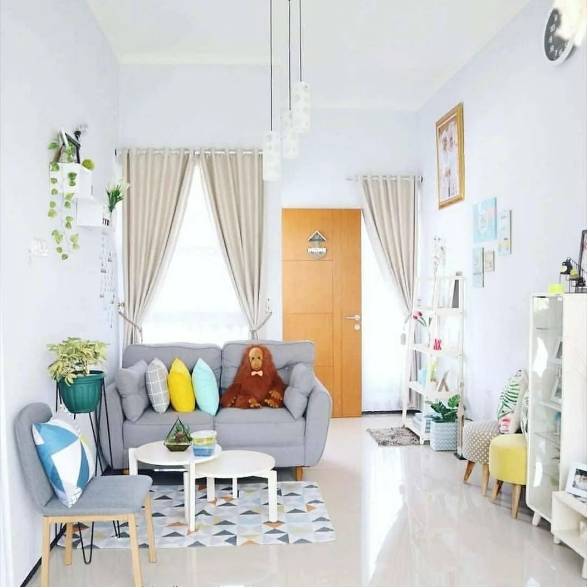 Ruang tamu mungil gaya Skandinavia dengan sofa abu-abu, bantal kuning cerah, dan rak pajangan minimalis.