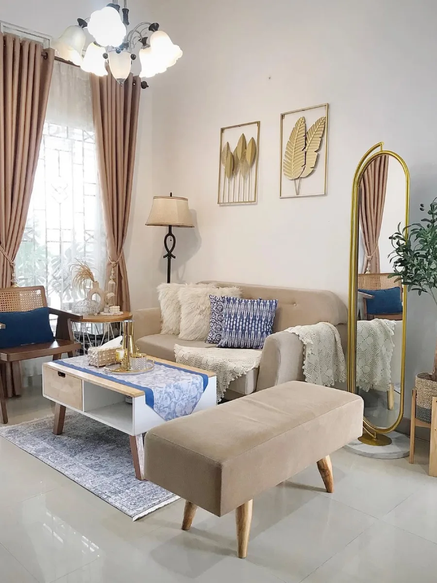 Dekorasi ruang tamu estetik nuansa krem dengan cermin berdiri bingkai emas dan hiasan dinding logam bentuk daun.