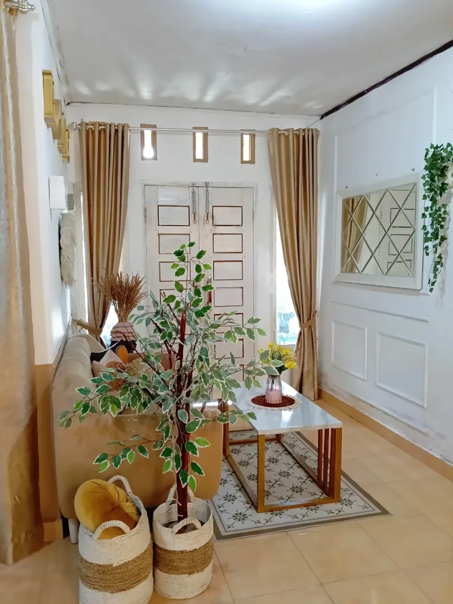 Ruang tamu minimalis elegan bernuansa beige dengan gorden emas, dinding aksen profil kayu (wainscoting), cermin geometris, dan tanaman hias tinggi di samping sofa.