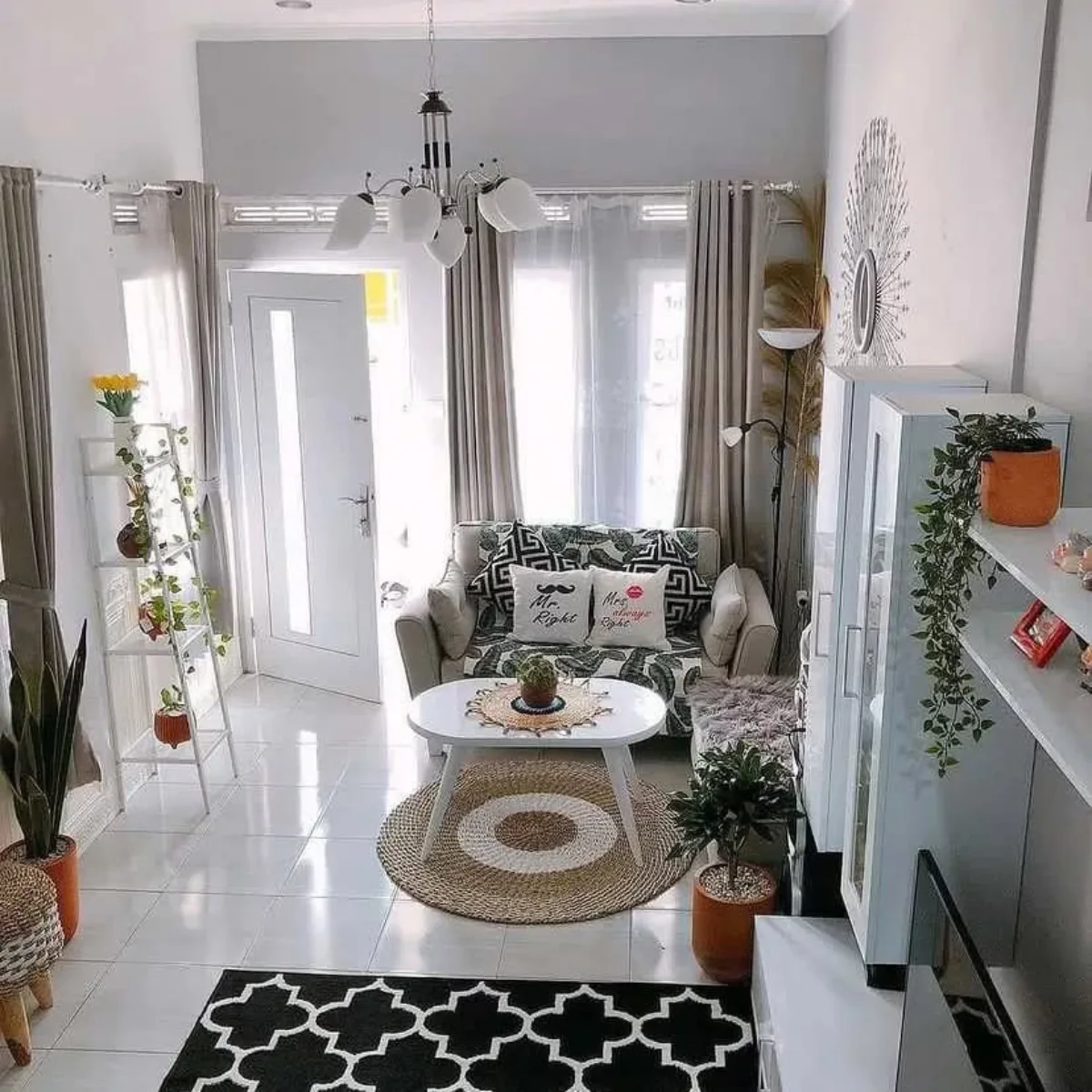 Ruang tamu minimalis yang terang benderang dengan pintu kaca lebar, sofa krem, dan rak tanaman putih.