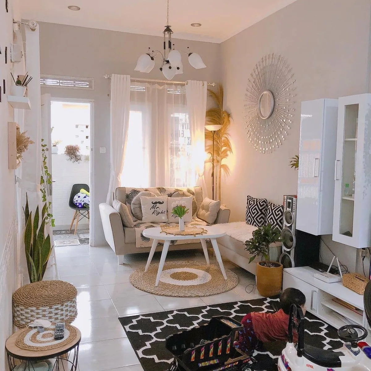 Ruang tamu modern dengan dekorasi cermin matahari besar di dinding dan karpet motif geometris hitam putih.