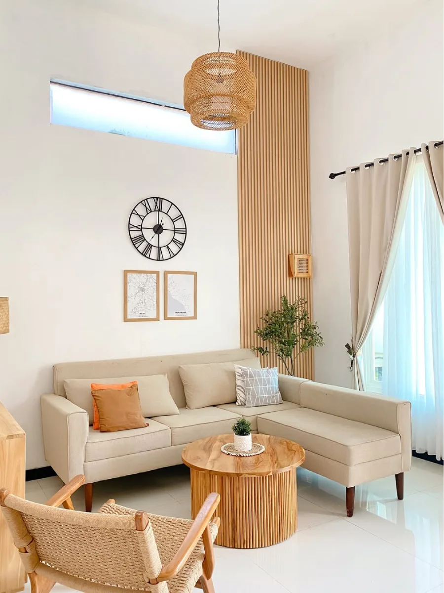 Desain ruang tamu gaya Japandi dengan panel dinding kayu vertical (slat wall), lampu gantung rotan, dan sofa L warna krem.