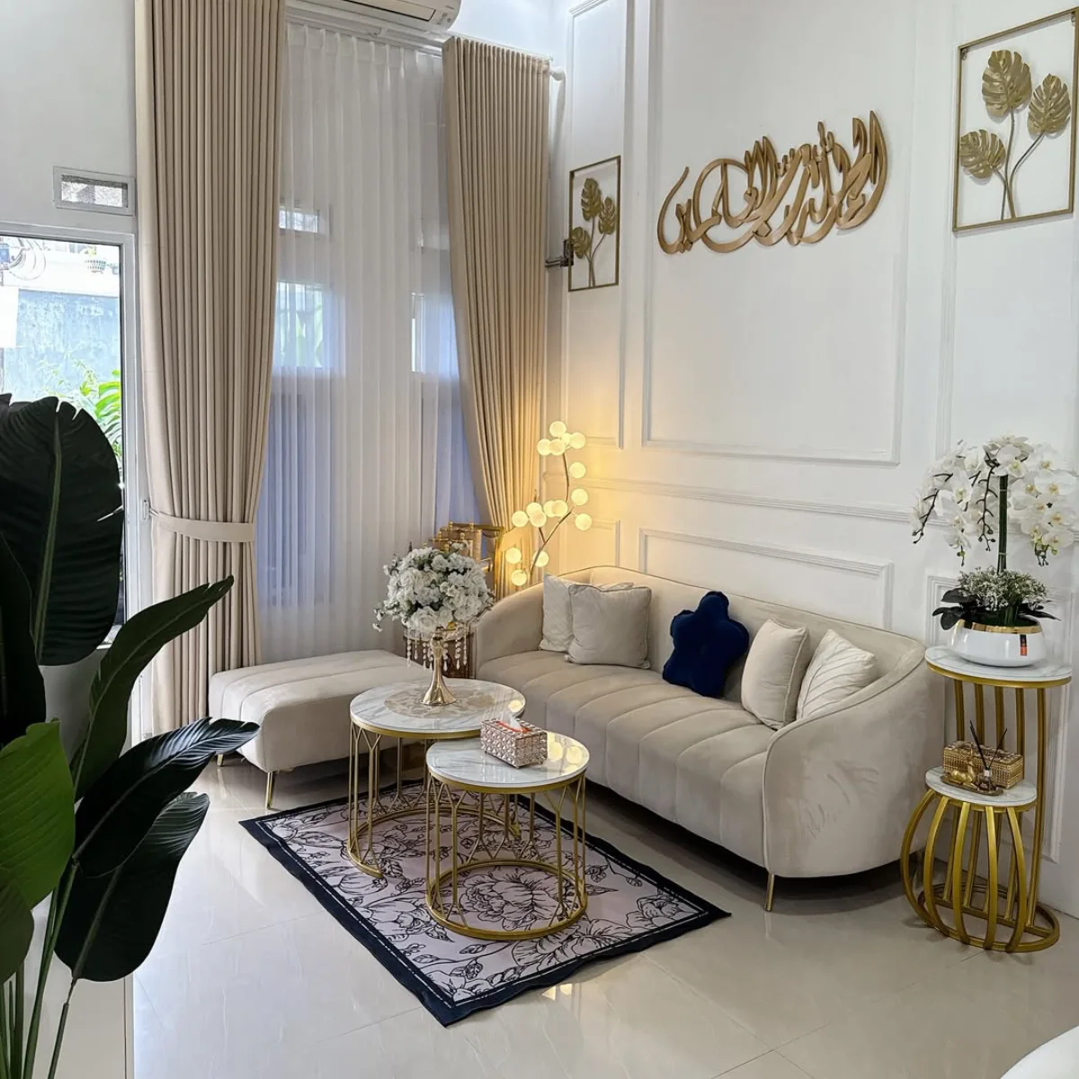 Inspirasi ruang tamu elegan nuansa krem beige dengan sofa melengkung, meja tamu marmer bulat, dan hiasan kaligrafi emas.