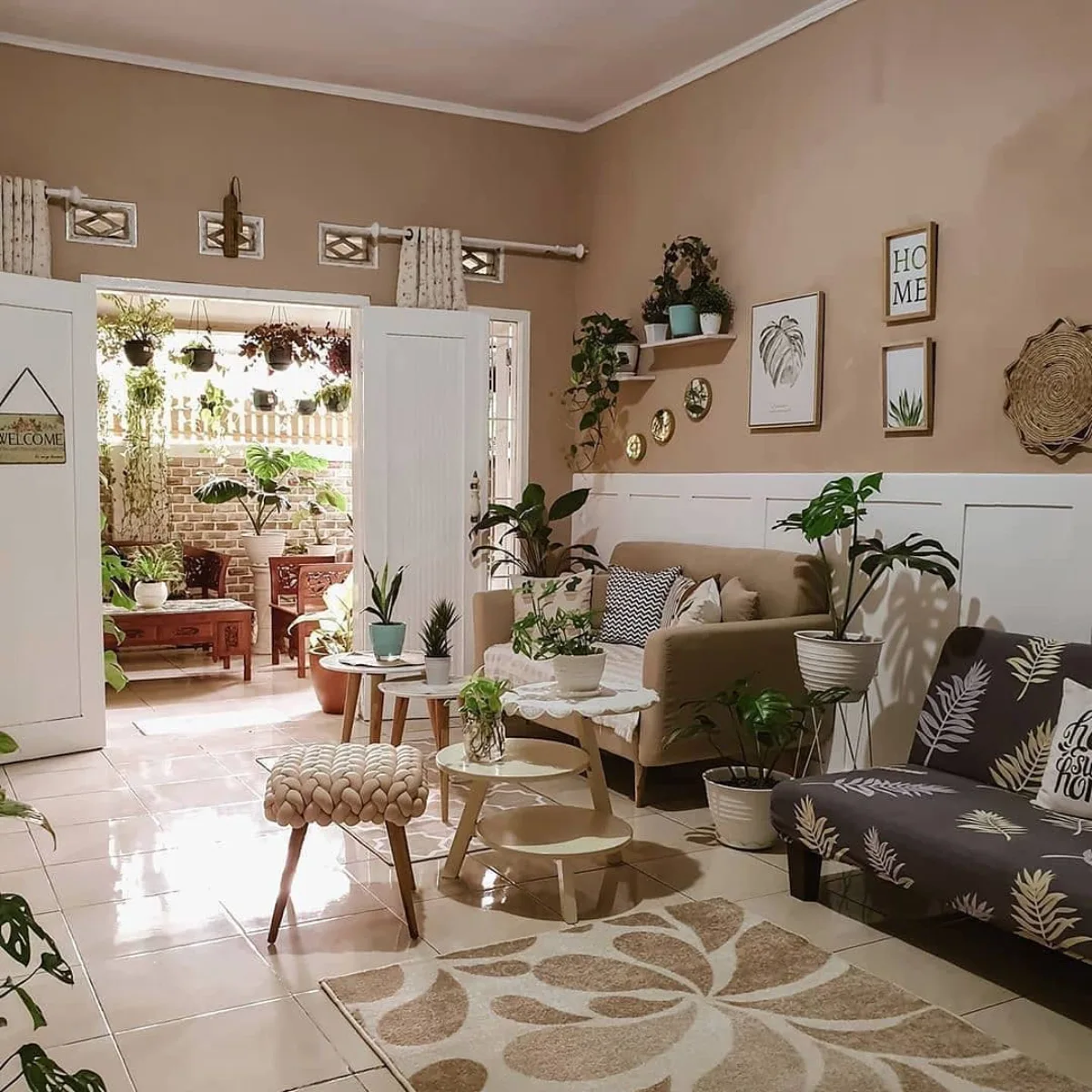 Ruang tamu bergaya boho dengan banyak tanaman hias di dalam ruangan dan pencahayaan alami yang terang.