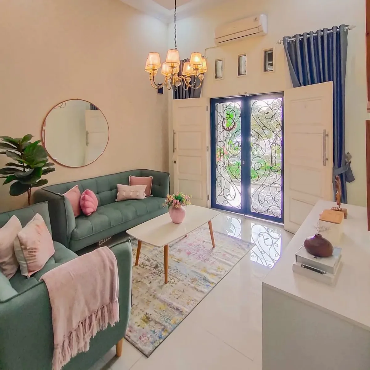 Ruang tamu minimalis dengan sofa hijau sage, meja putih mungil, dan cermin bulat besar di dinding.