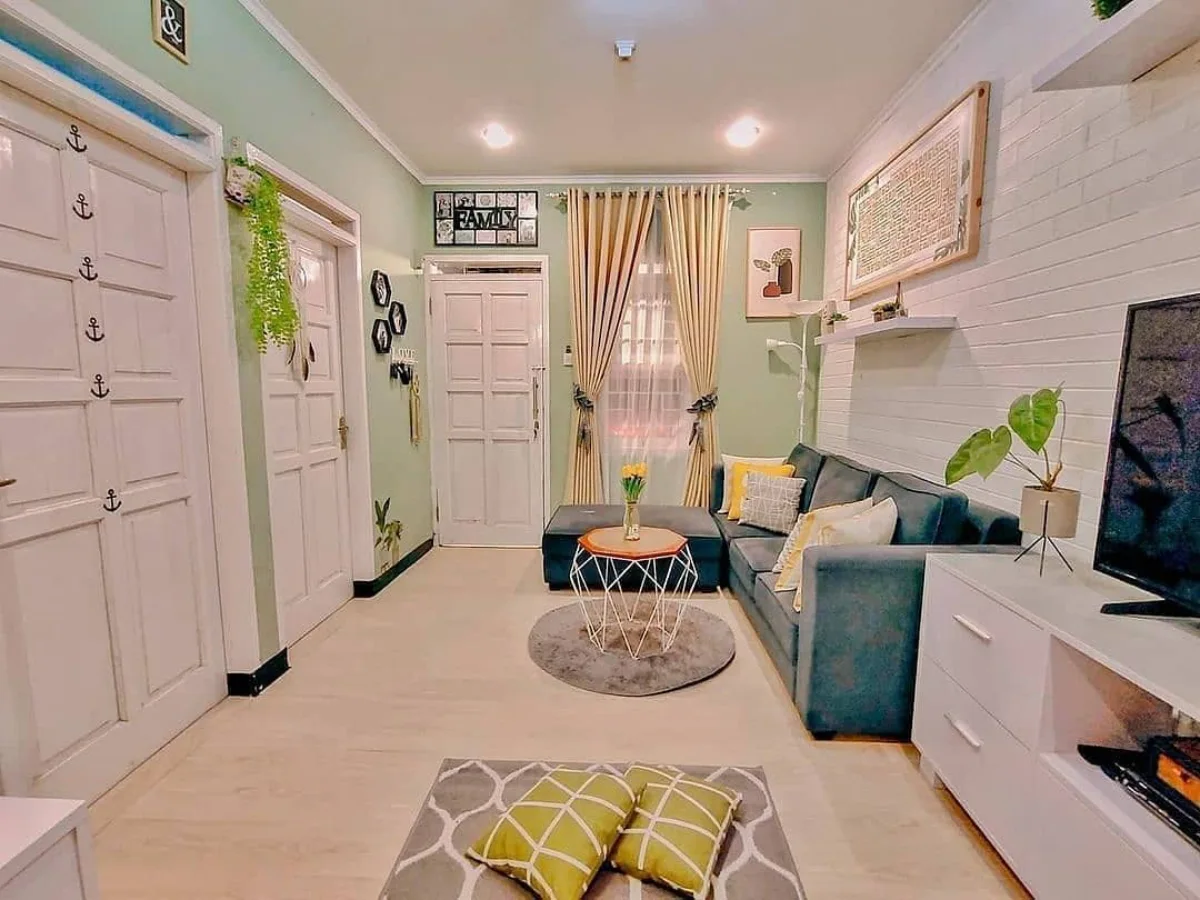 Desain ruang tamu bertema hijau sage dengan sofa abu-abu dan dekorasi dinding minimalis yang rapi.