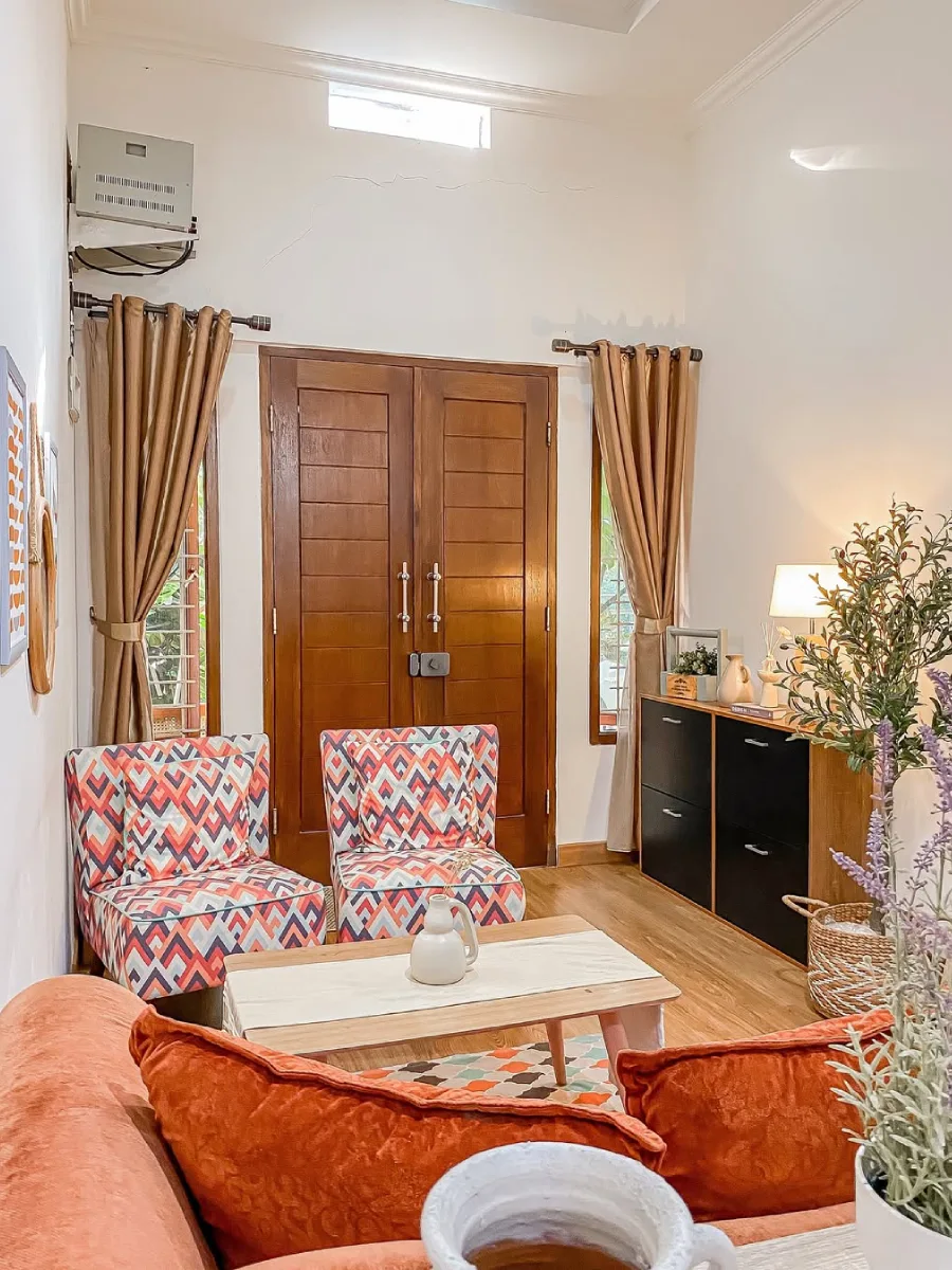 Ruang tamu gaya eklektik dengan kursi santai motif geometris warna-warni dan pintu kayu jati besar.