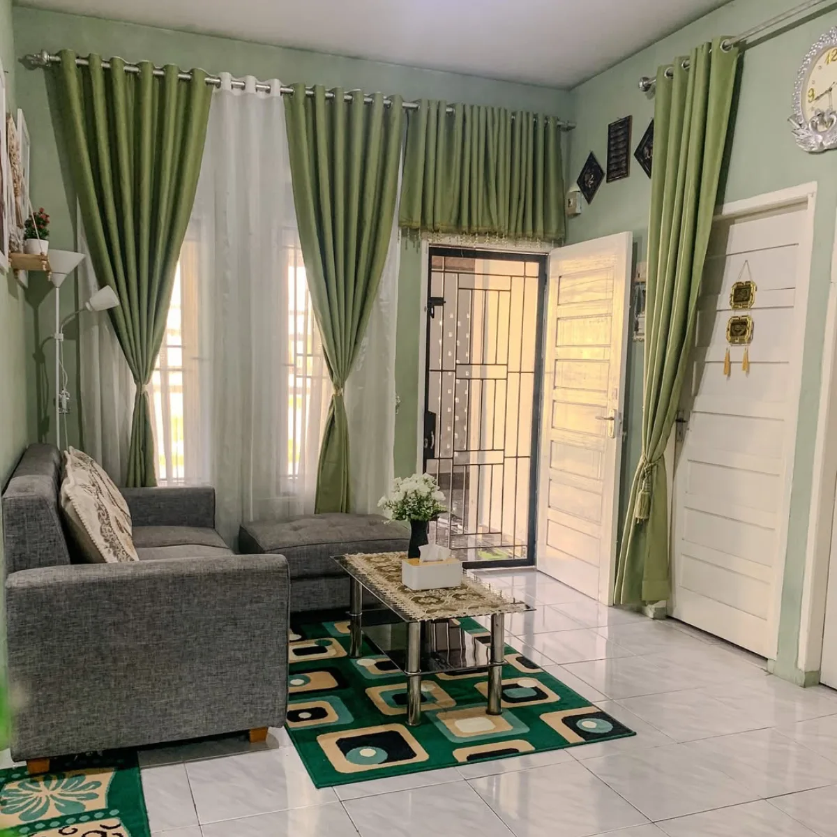 Ruang tamu minimalis segar nuansa hijau sage dan abu-abu dengan gorden tinggi dan karpet geometris hijau.