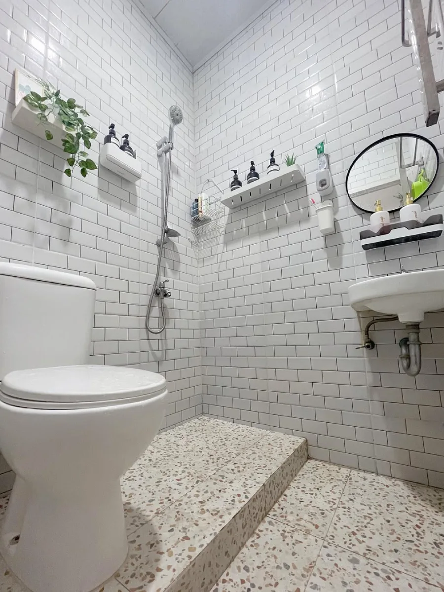 Tampilan sudut rendah desain kamar mandi minimalis modern 1.5 x 1.5 meter yang estetik, menampilkan lantai terrazzo cokelat muda yang senada dengan dinding putih bersih untuk kesan luas.