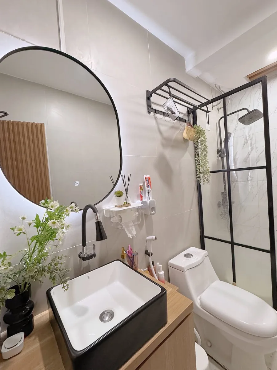 Desain kamar mandi minimalis modern berukuran 1.2 x 2.7 meter yang dilengkapi wastafel kotak hitam, cermin bulat besar dengan backlight LED, serta partisi shower kaca berbingkai hitam yang elegan.
