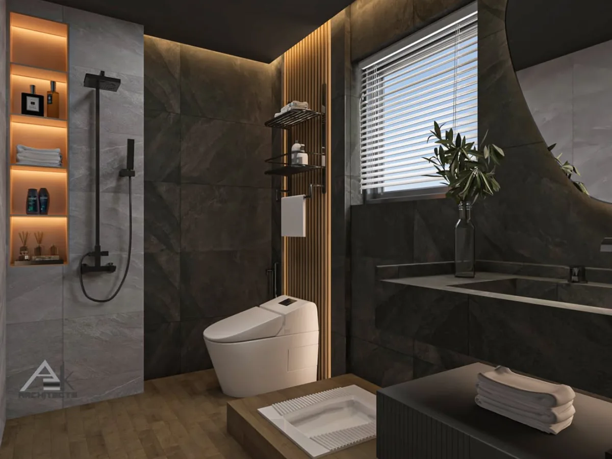 Tampilan detail area shower dan toilet pada kamar mandi bernuansa gelap. Rak dinding vertikal dengan lampu latar oranye hangat memajang perlengkapan mandi. Terlihat perpaduan tekstur batu alam gelap pada dinding dan lantai kayu parket, serta jendela kecil dengan tirai putih.