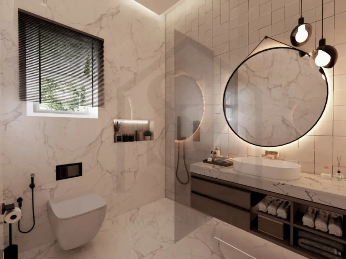 Kamar mandi bernuansa putih bersih dengan ubin marmer carrarra, cermin bulat besar yang digantung dengan strap hitam, lampu gantung bola industrial, dan jendela dengan tirai venetian blinds hitam.