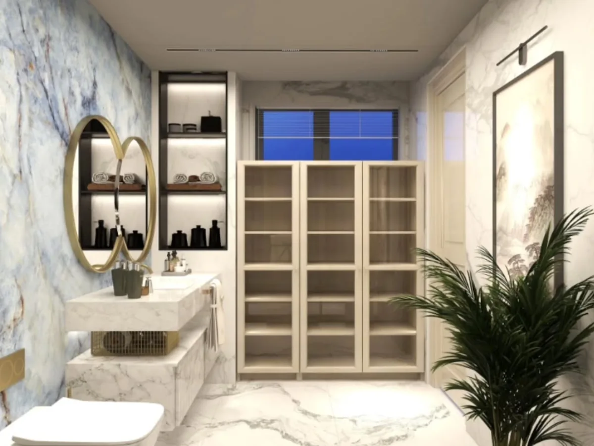 Sudut area penyimpanan di kamar mandi mewah, menampilkan lemari kaca tinggi berwarna krem dengan rak terbuka, lukisan vertikal di dinding, tanaman hias besar dalam pot, dan lantai marmer putih dengan corak abu-abu.